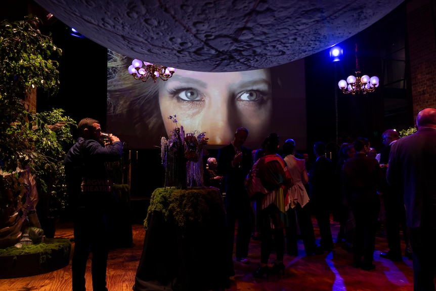 A blown up image of Anne Edmonds' Bad Company character is seen with a group of people in front at event.