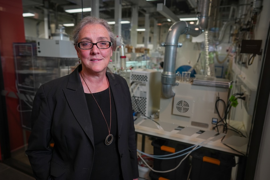 A smiling woman in a laboratory wearing glasses.