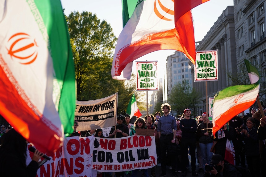 Anti-war protesters wave flags and hold banners as they march down a city street.