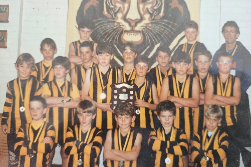 A football team of boys in striped jumpers, including AFL star Buddy Franklin, wearing medals from a win in 1997