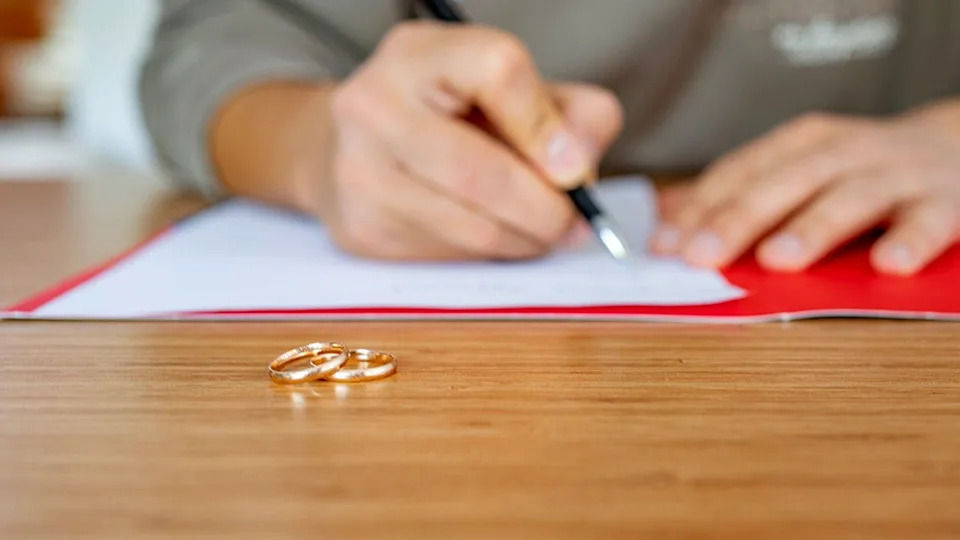 Husband writing divorce petition at home with two wedding rings on table