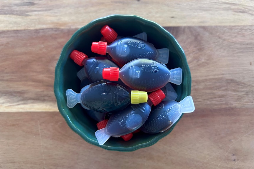 A green bowl of small plastic fish filled with soy sauce, on a wooden surface.