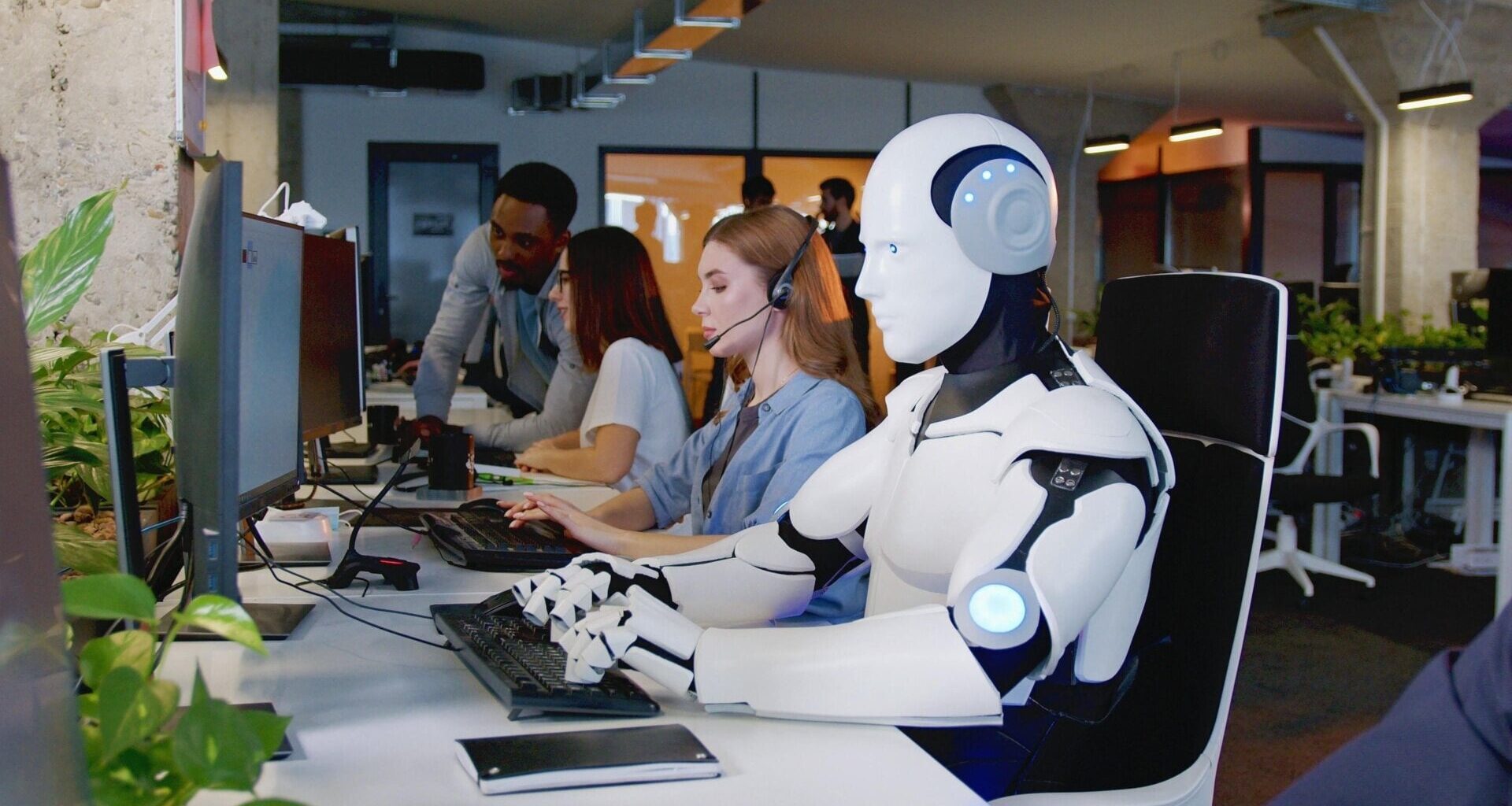 A humanoid robot typing at a keyboard in an office.