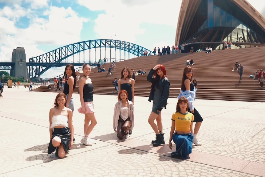 Eight girls pose for a photo with the Sydney Harbour Bridge and opera house in the background.