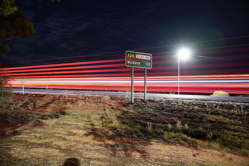 Light trails made by truck lights sit behind a green road sign reading Sturt Highway.