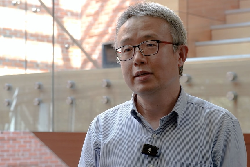 A grey-haired man in glasses in a large building.