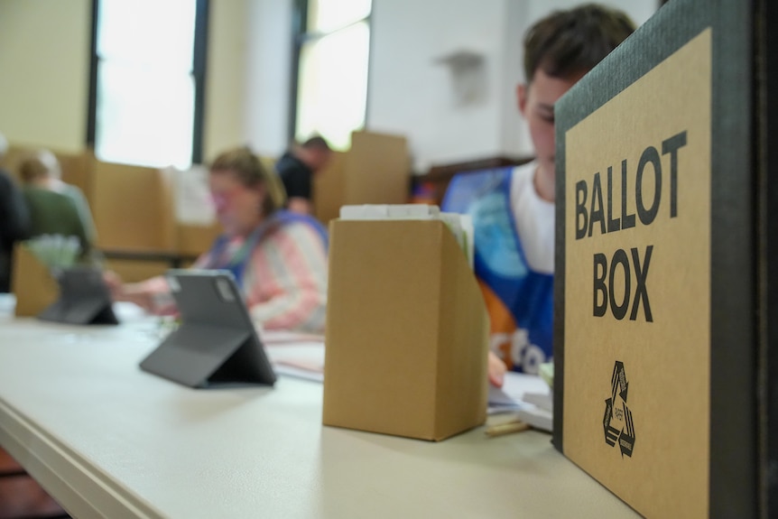 A brown cardboard box with the words BALLOT BOX on it on a desk 