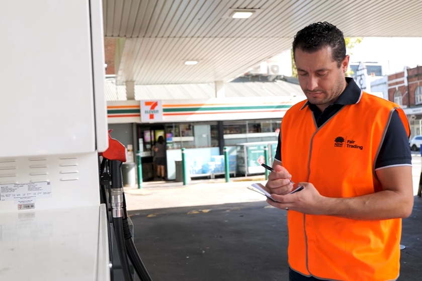 A man in an orange hi-vis shirt inspects pricing at a fuel bowser. 