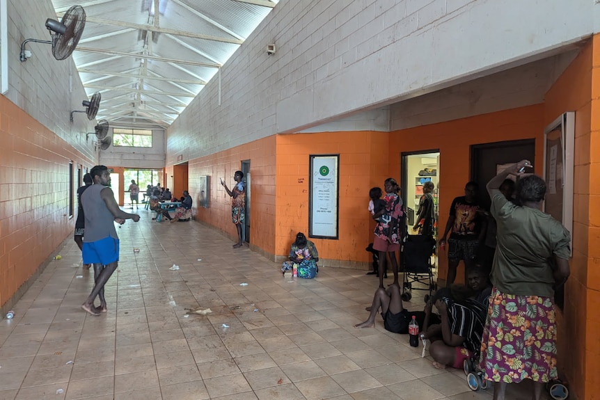 A hallway with a group of people lining up outside a door.