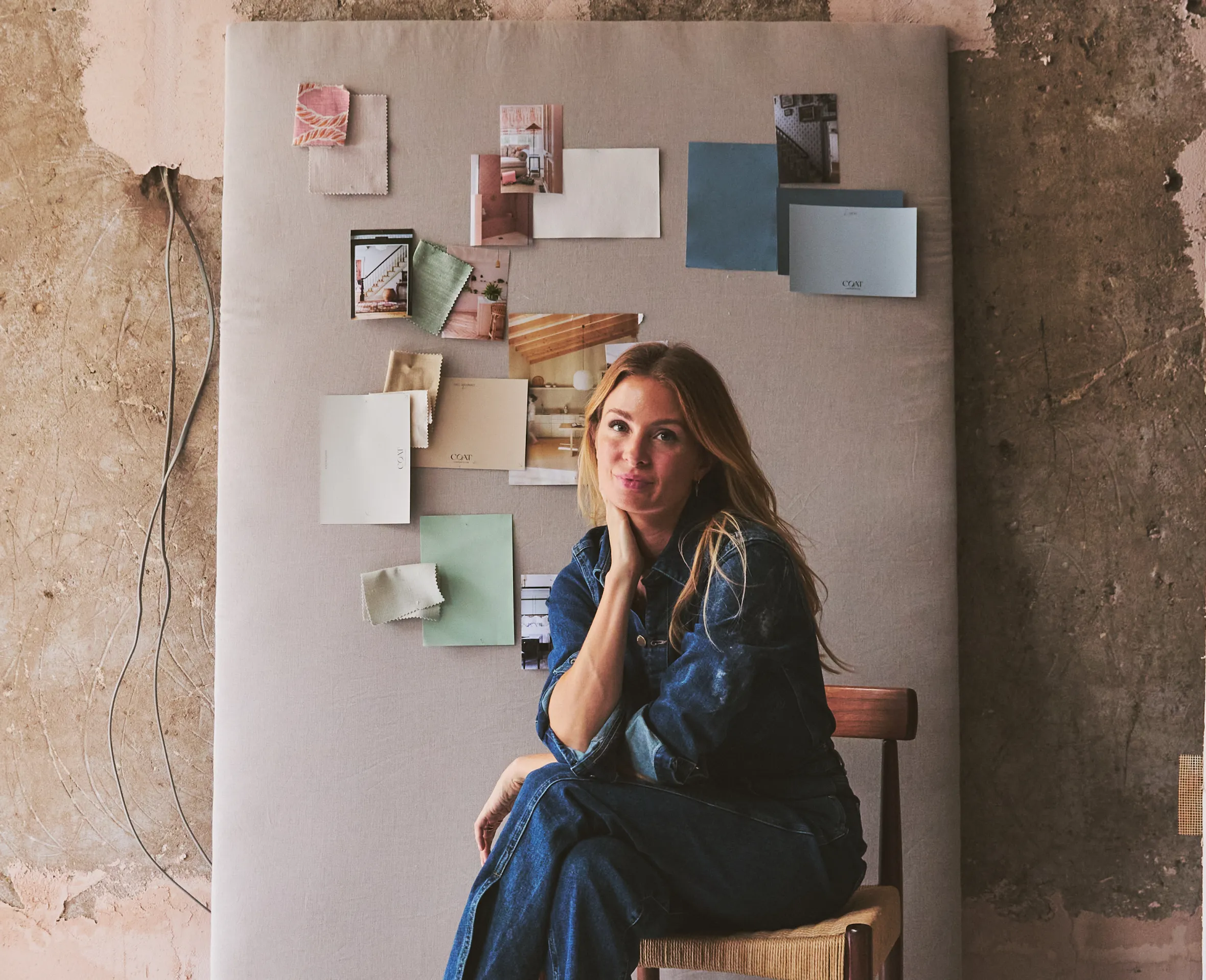Millie Mackintosh sitting on a chair in a room undergoing renovation, with paint color swatches and design photos on a board behind her.