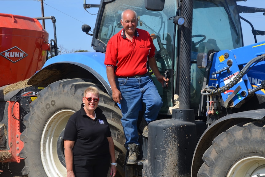 A farming couple stand in front of a tractor
