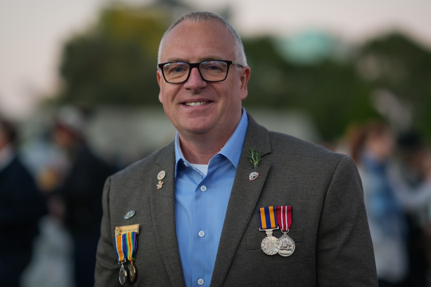 Man wearing glasses and suit jacket with military medals either side of chest 