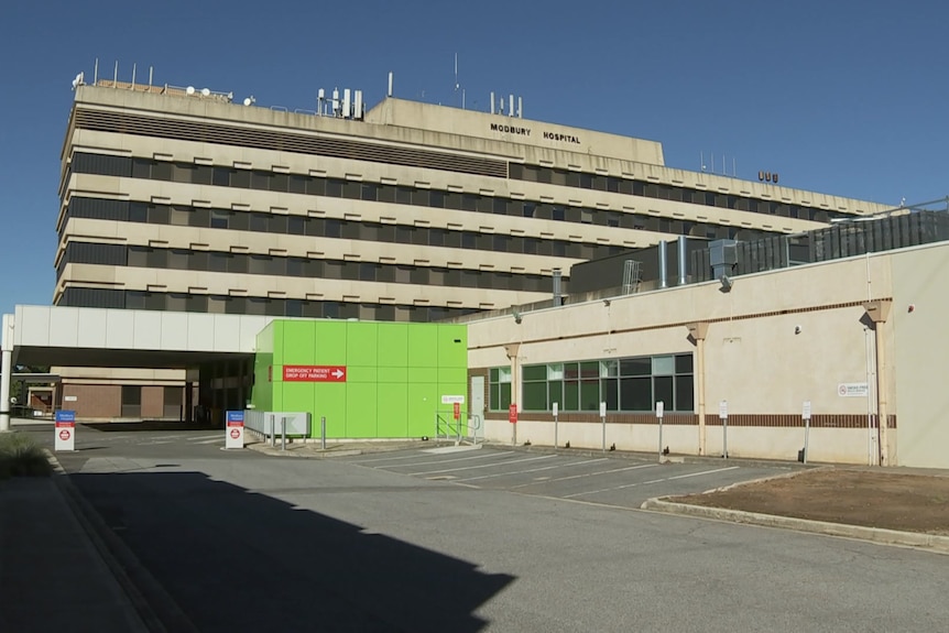 An empty car park in front of a six-storey building and emergency department entrance.