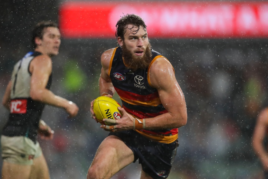 Riley Thilthorpe of the Crows running with the ball as rain falls during an AFL match