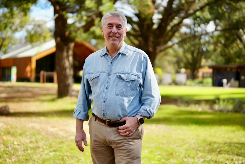 A man with grey hair stands smiling for the camera. 