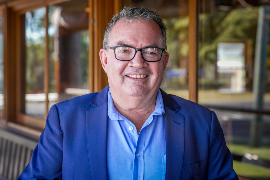 A man wearing a collared shirt and suit jacket, smiling.