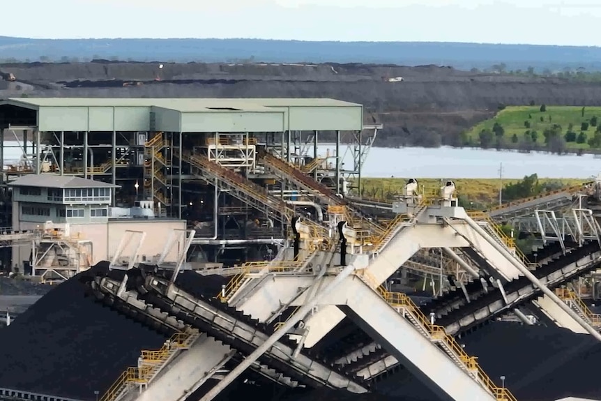 Conveyor belts, a tailings dam and mounds of coal at a mine site.