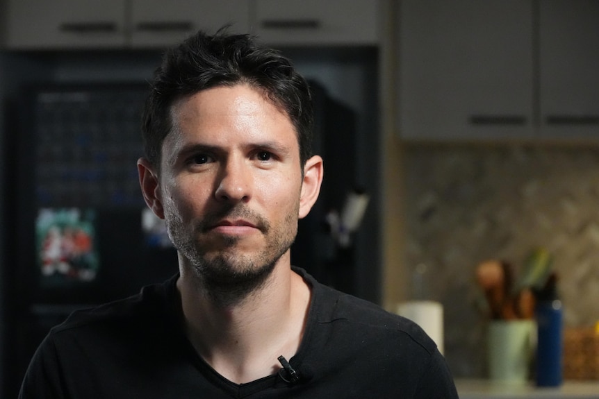 A close up photo of a man with dark hair, wearing a black top