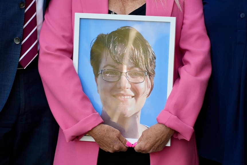 A picture in a frame of Kelly T'Hart, being held by a woman wearing a pink blazer. 