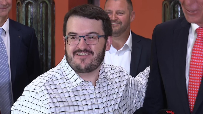 A man with a beard and glasses puts his arm around a much taller man. 