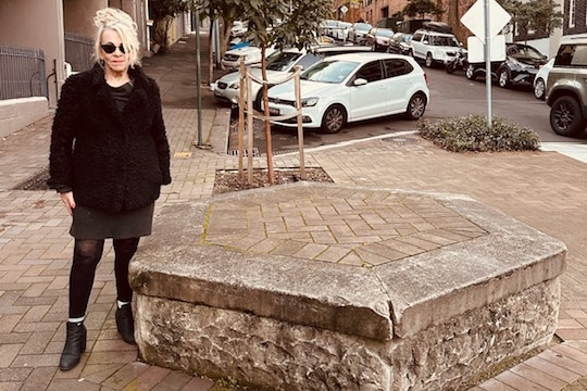 A woman dressed in blank stand next to an empty plinth.
