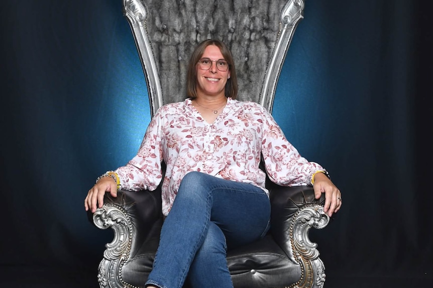 A woman sitting in a large chair in jeans and blowse smiling for the camera