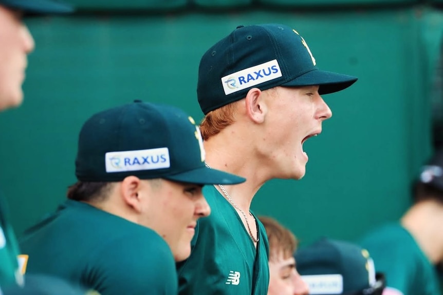 A young man in a green baseball uniform yells from the sidelines