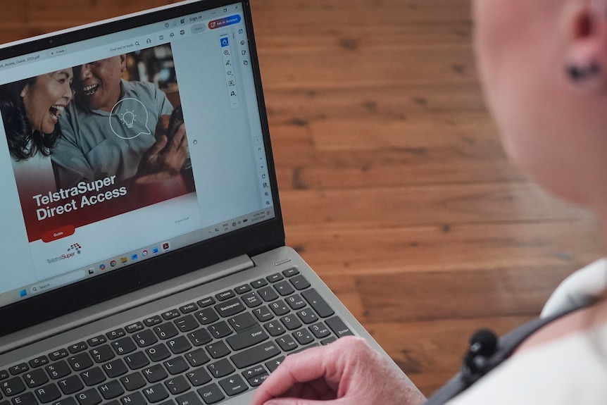 A person sits at a laptop displaying a superannuation product webpage.