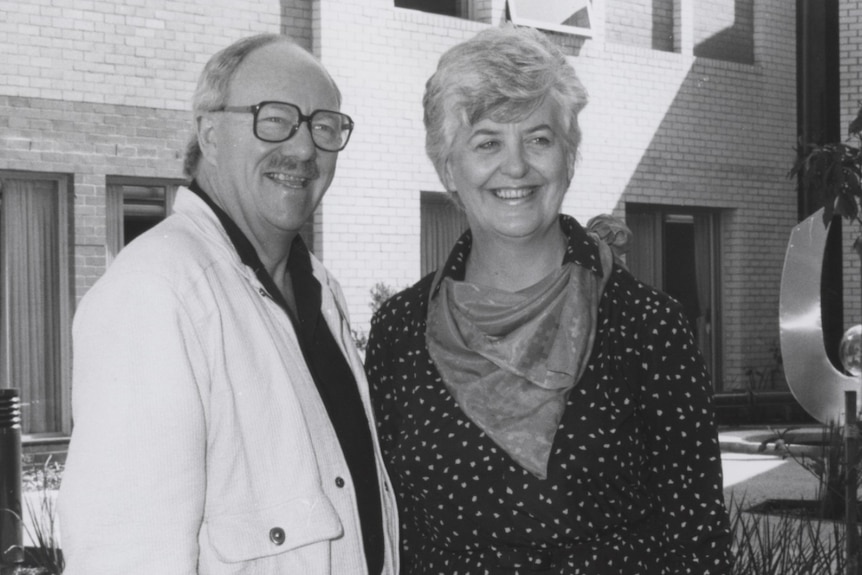 A black and white photo of John Clark and Elizabeth Butcher standing outside a brick building.