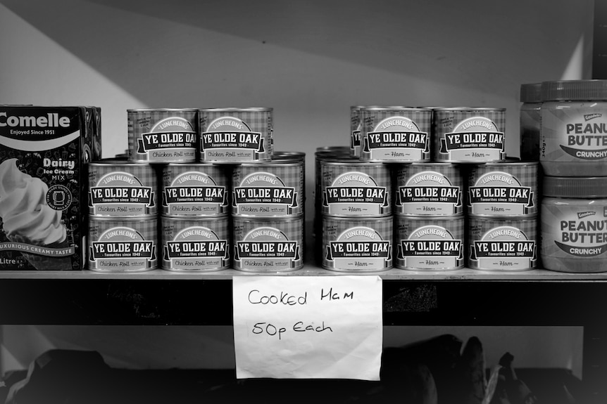 A shelf with tins of cooked hams and a sign advertising them for 50p each.