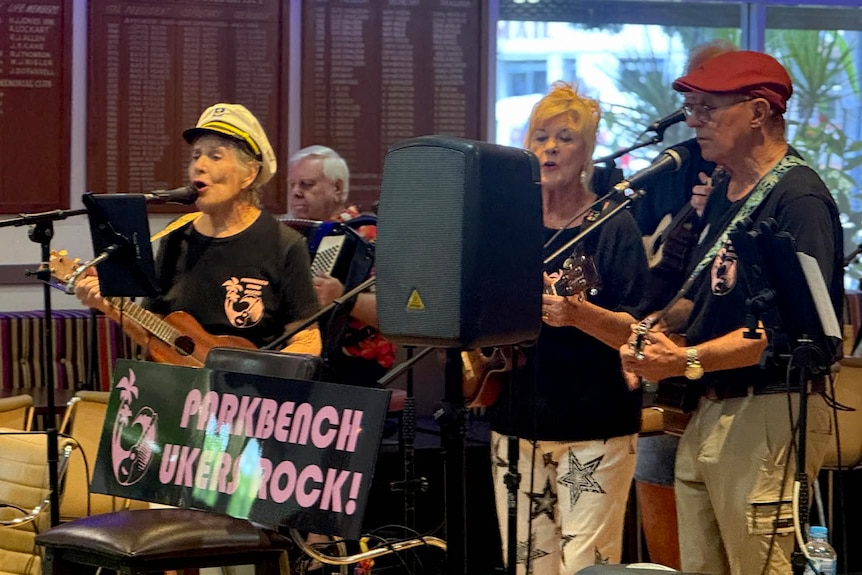 Three people on stage playing ukuleles to a crowd.