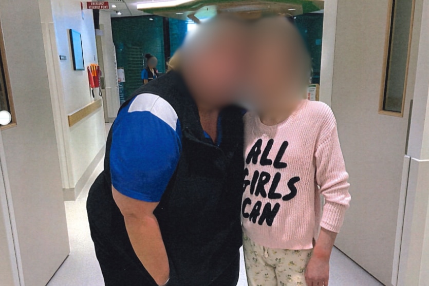A woman and a girl in a hospital hallway with their faces blurred out.
