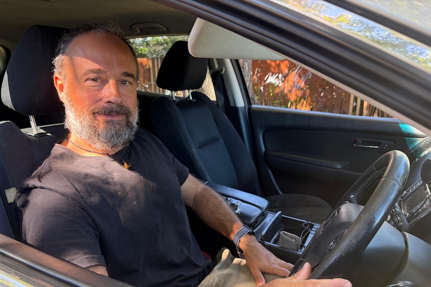 A man with grey hair and a beard sitting in the front seat of a vehicle.