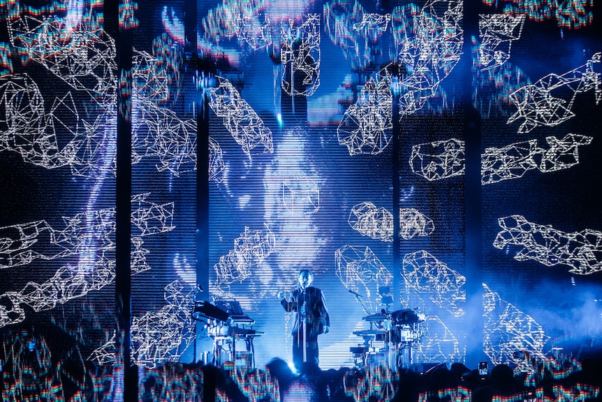 Thom Yorke performs live at Sydney Opera House forecourt, surrounded by on-screen visuals of cgi boxes.