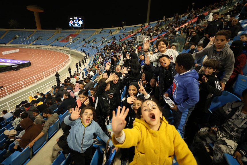 A group of young people in stadium seating cheer for the camera.