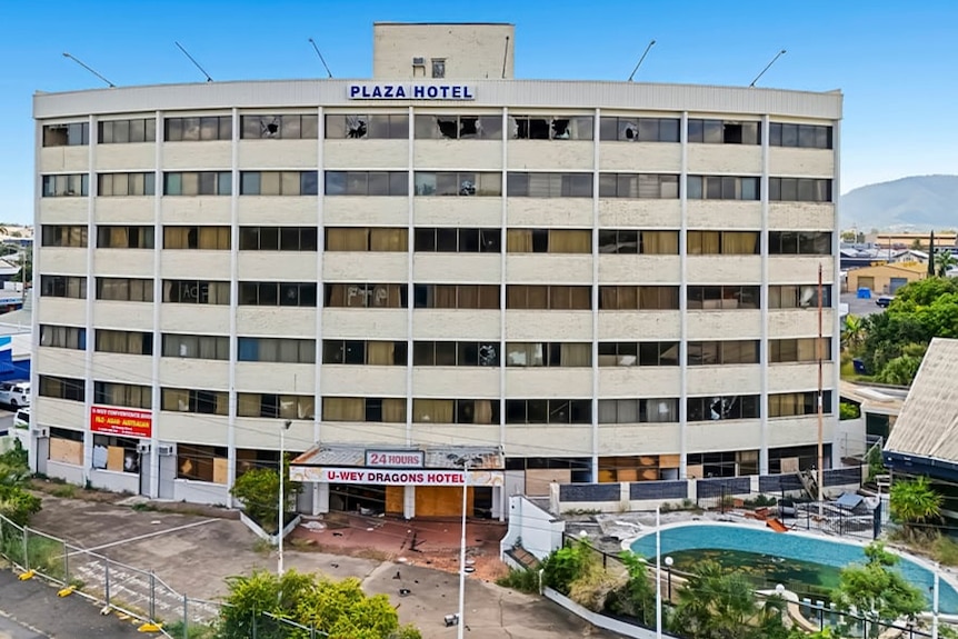 A multi-storey concrete building with smashed windows, boarded -up doors and rubbish strewn around it.