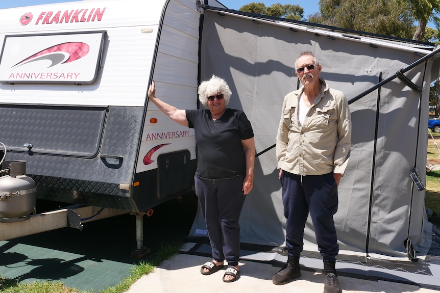 A medium shot of two people standing in front of a caravan