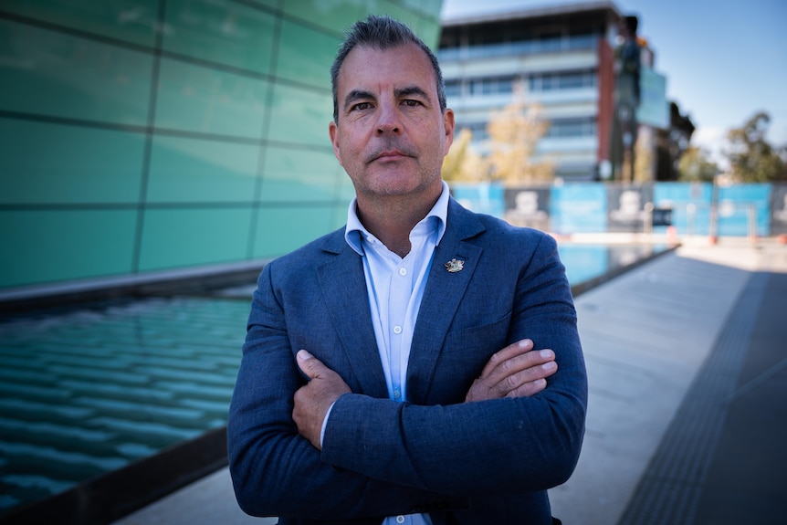 A man in a suit jacket stands in front of a building.