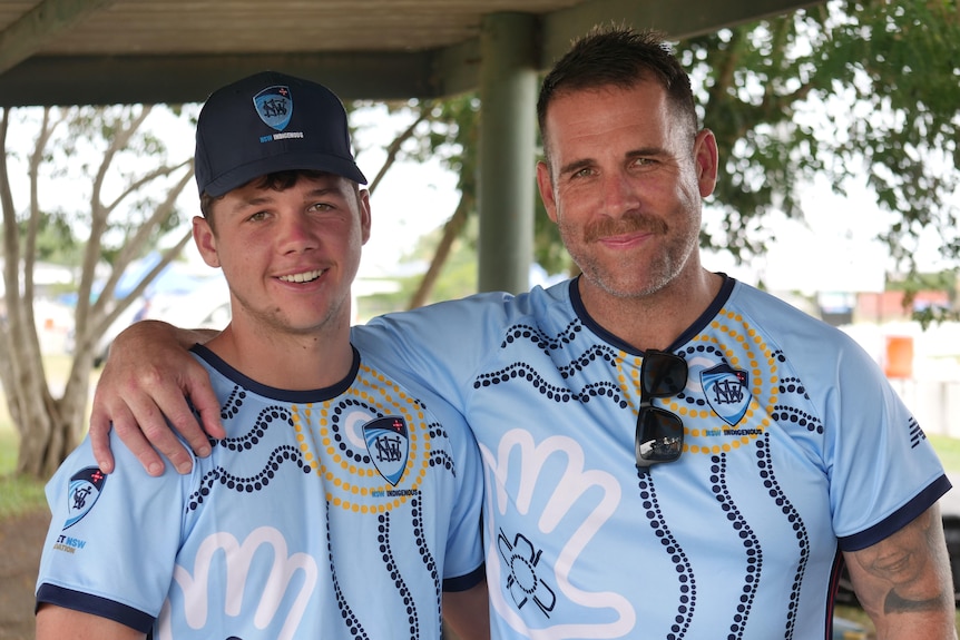 A man and his son smiling at the camera, standing next to each other