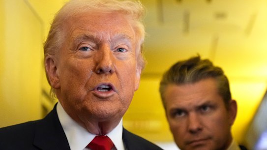Donald Trump speaks to reporters as US Defence Secretary Pete Hegseth listens while travelling aboard Air Force One.