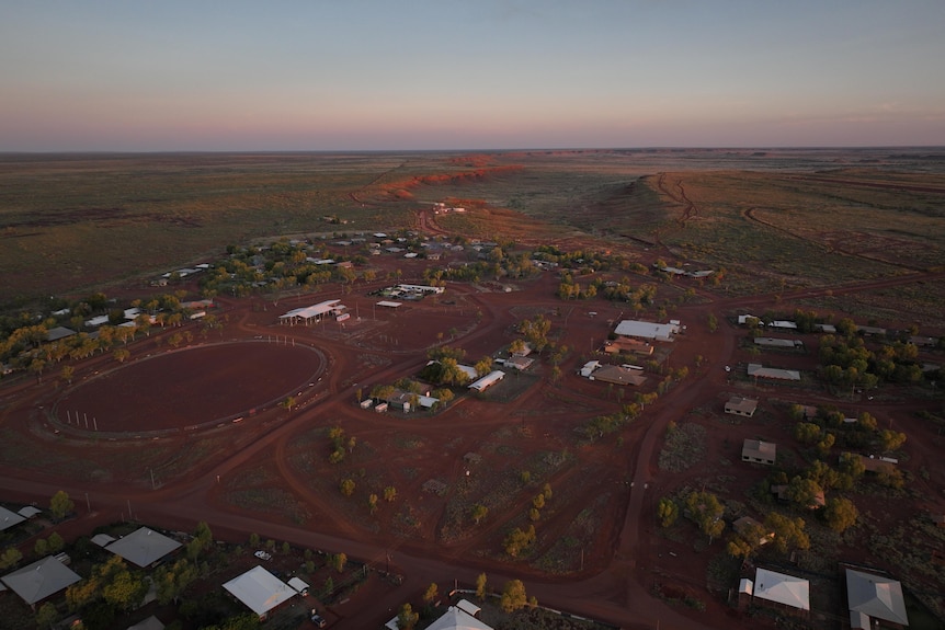 A drone shot from above showing the community of Balgo's few houses on red land near a vast escarpment.