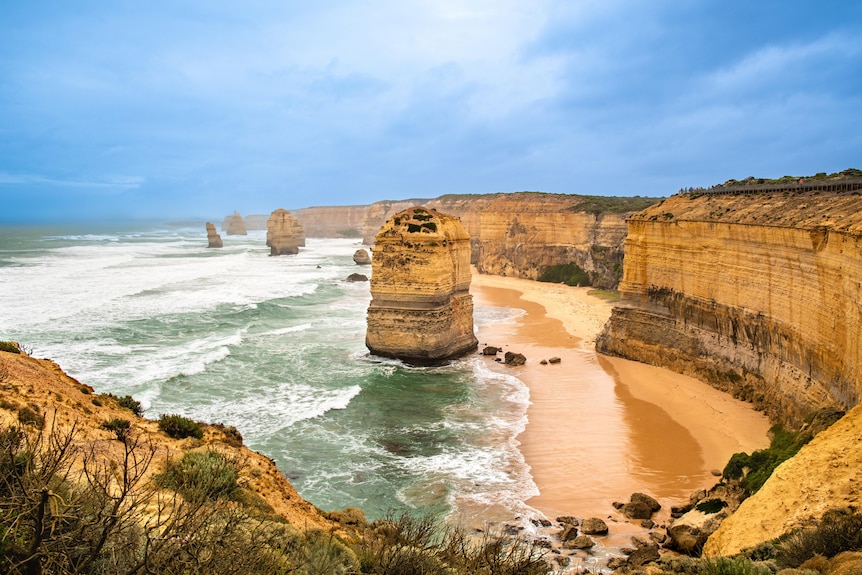 A view down at coastal yellow cliffs stretching into the distance and large limestone monoliths in beach tides.