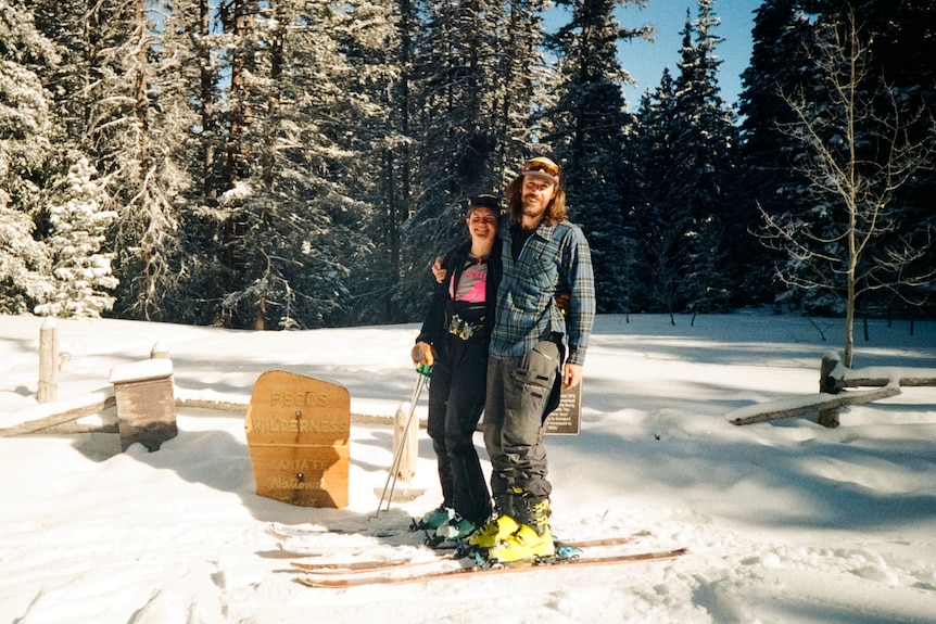 A couple stands together with arms around each other while on skis in the snow.