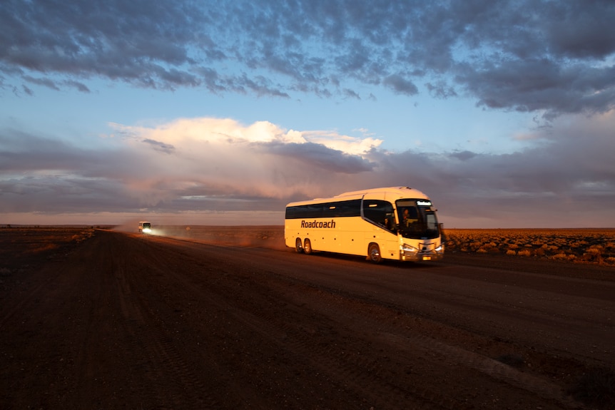 A large bus travels on an empty outback road.