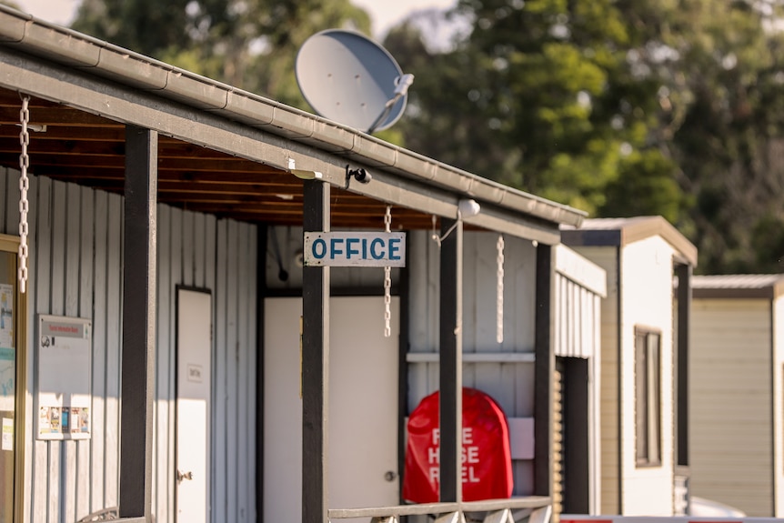 A building with a sign hanging in front reading 'office', in the background there are accommodation units.