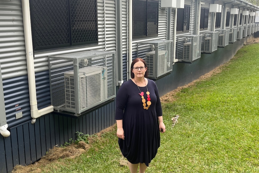 A woman in a black dress stands in front of demountable buildings