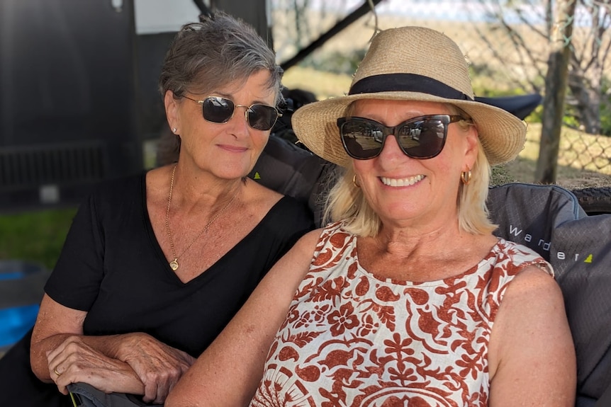 Two women smile sitting side by side in caming chairs outside.
