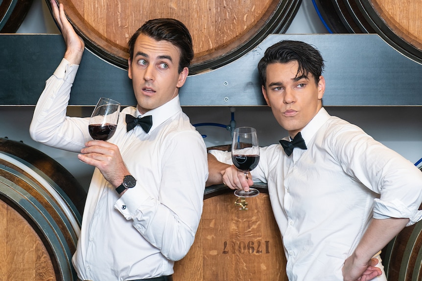 Two men in white button downs hold glasses of red wine