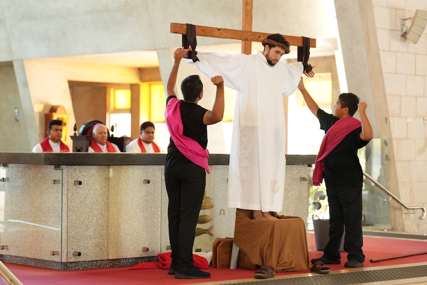 A man dressed as jesus stands upon a cross