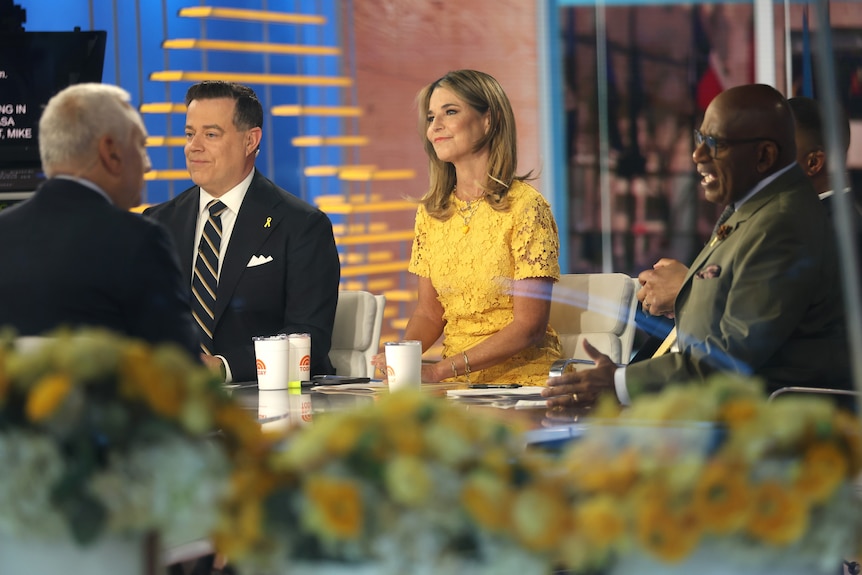 news anchors sit smiling at desk, wearing yellow